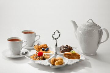 Close up view of dessert plate, china teapot and cups on white background