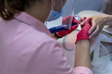 A woman sits at a table and gives a manicure to client.A manicure master in a pink robe, a protective screen and a mask.Personal protective equipment of the beauty master.Women's manicure.