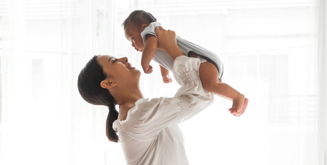 Portrait of enjoy happy love family asian mother playing with adorable little asian baby.Mom touching with cute son moments good time in a white bedroom.Love of family concept