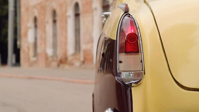 close up view of taillight of old retro vintage car in beige and burgundy colors. car is parked in front of red brick building.