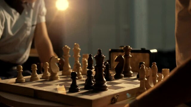 People play chess in a dark room with warm lighting. Close-up 