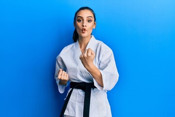 Beautiful brunette young woman wearing karate fighter uniform with black belt doing attack pose making fish face with mouth and squinting eyes, crazy and comical. © Krakenimages.com
