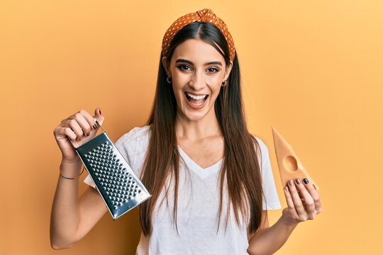 Beautiful brunette young woman holding grater and cheese smiling and laughing hard out loud because funny crazy joke.