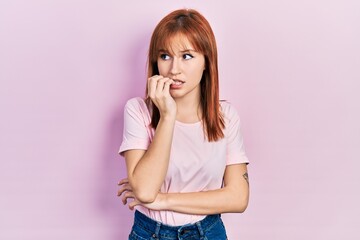 Redhead young woman wearing casual pink t shirt looking stressed and nervous with hands on mouth biting nails. anxiety problem.