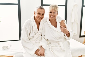 Senior caucasian couple smiling happy and hugging sitting on massage table at beauty center.