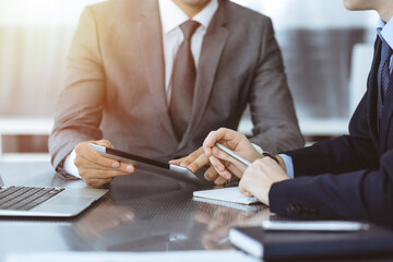 Unknown businessman using tablet computer and working together with his colleague while sits at the glass desk in modern office. Teamwork and partnership concept