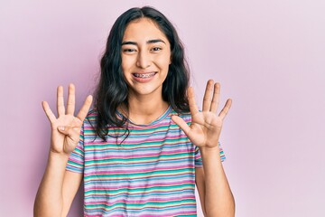 Hispanic teenager girl with dental braces wearing casual clothes showing and pointing up with fingers number nine while smiling confident and happy.