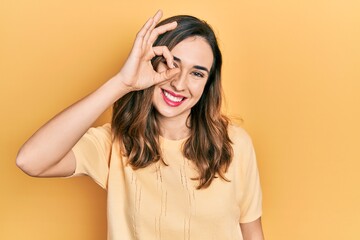 Young hispanic girl wearing casual clothes smiling happy doing ok sign with hand on eye looking through fingers