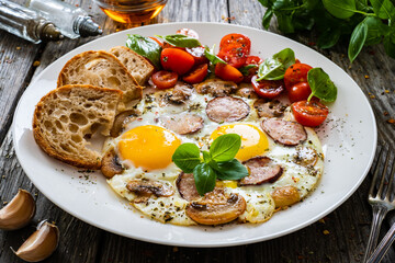 Continental breakfast - sunny side up eggs, bread and fresh vegetables on wooden table
