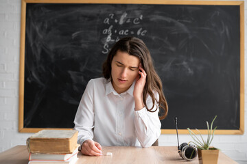 class teacher sitting in front of the blackboard holds his head with his hands and suffers from...