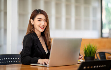 Portrait of Confident asian young business woman working on laptop at her workplace at modern office.Blurred background