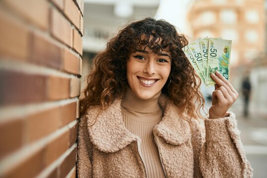 Young hispanic woman smiling happy holding israel shekels banknotes at the city