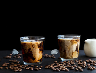 Two glass iced coffee with cream, ice cubes and coffee beans on dark background with copy space. Refreshing drink.