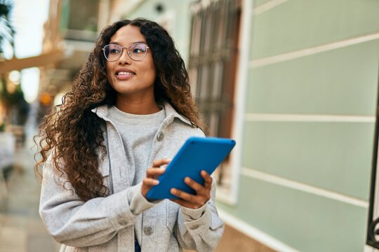 Young latin woman smiling happy using touchpad at the city.