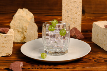 a clear glass with ice on a white plate. Ice and gooseberries. Ice in a glass among the stones.