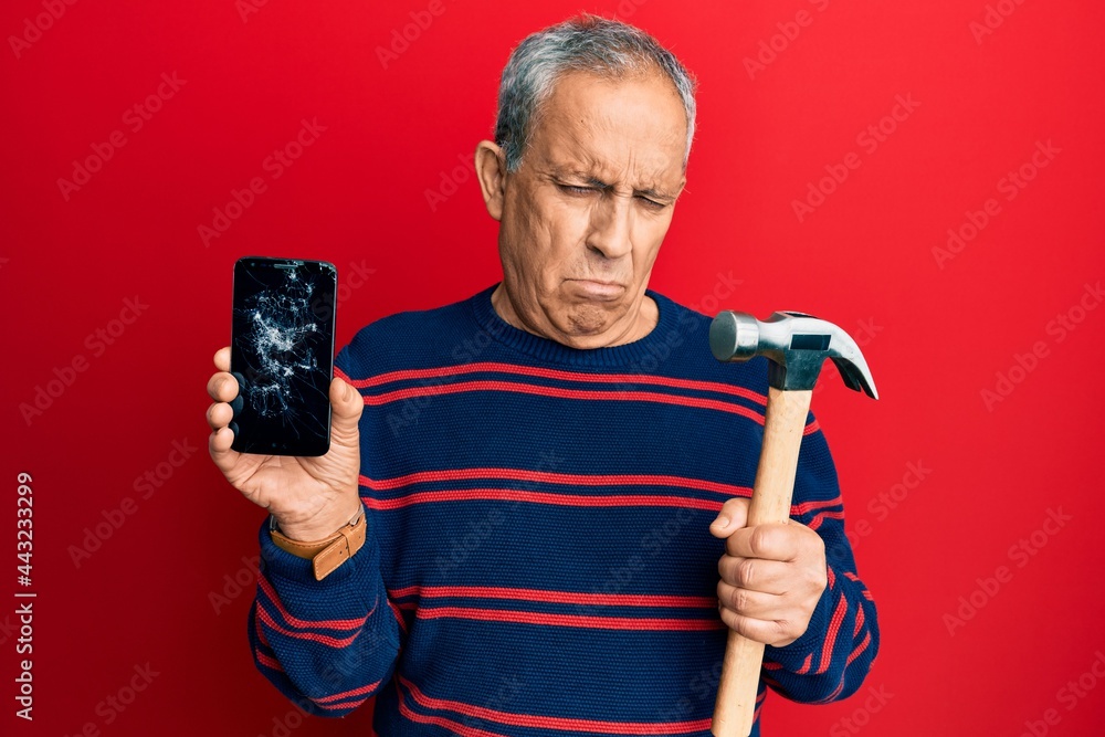 Canvas Prints senior hispanic man holding broken smartphone showing cracked screen and hammer depressed and worry 