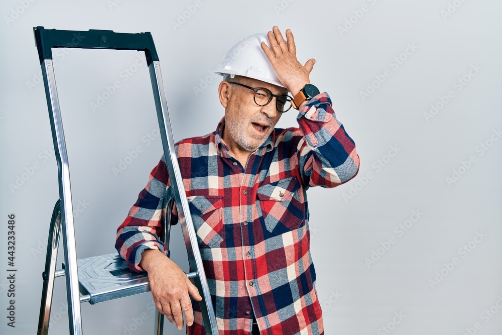 Poster handsome mature handyman close to construction stairs wearing hardhat smiling confident touching hai