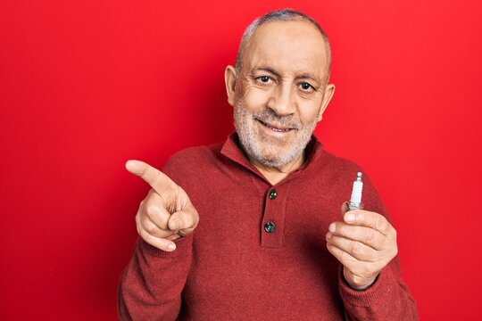 Handsome mature man holding spark plug smiling happy pointing with hand and finger to the side
