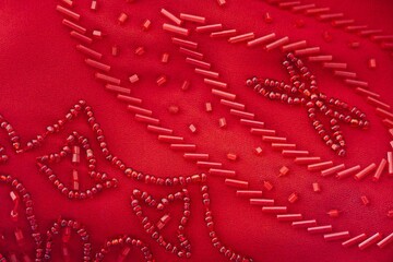 Red beaded fabric. Closeup of hand-made textile clothing decoration and bead embroidery. Fancy...
