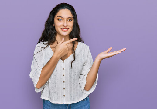 Brunette young woman wearing casual clothes amazed and smiling to the camera while presenting with hand and pointing with finger.