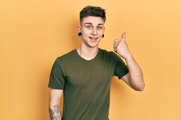 Young caucasian boy with ears dilation wearing casual green t shirt smiling happy and positive, thumb up doing excellent and approval sign