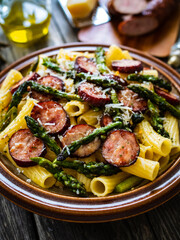Tortiglioni with sausages, parmesan and asparagus on wooden table
