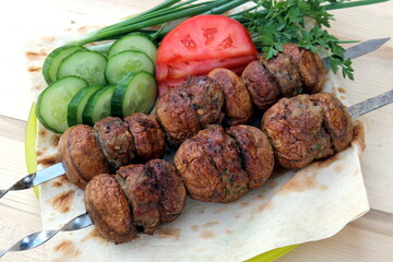 Mushrooms stuffed with minced meat, planted on skewers and fried on the grill lie on pita bread with vegetables