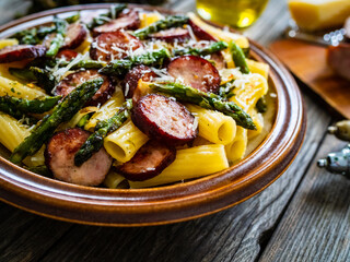 Tortiglioni with sausages, parmesan and asparagus on wooden table
