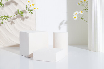 Empty podium or pedestal with chamomile flowers on a white background. Blank shelf product standing...