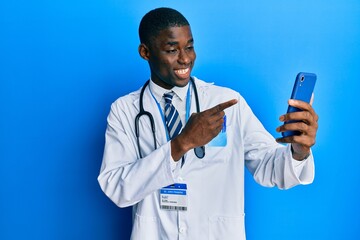 Young african american man wearing doctor uniform using smartphone smiling happy pointing with hand and finger