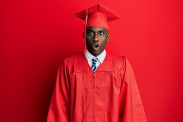 Young african american man wearing graduation cap and ceremony robe afraid and shocked with surprise expression, fear and excited face.