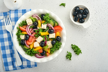 Traditional Greek salad of fresh cucumber, tomato, sweet pepper, lettuce, red onion, feta cheese and olives with olive oil on white plate. Healthy food, top view.