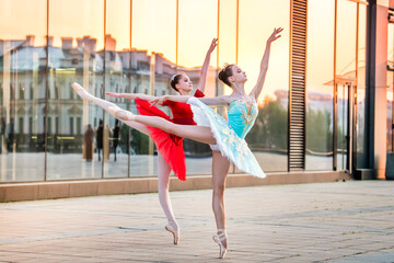 two young ballerinas in a bright red and blue tutu are dancing against backdrop of the reflection of city sunset - obrazy, fototapety, plakaty