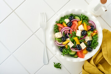 Traditional Greek salad of fresh cucumber, tomato, sweet pepper, lettuce, red onion, feta cheese and olives with olive oil on white plate. Healthy food, top view.