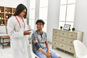 Obraz premium Young latin doctor woman smiling happy measuring pulse using tensiometer at the clinic.