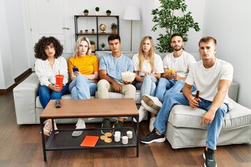 Group of people eating snack sitting on the sofa at home thinking attitude and sober expression looking self confident