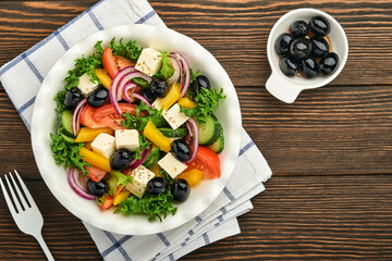 Traditional Greek salad of fresh cucumber, tomato, sweet pepper, lettuce, red onion, feta cheese and olives with olive oil on white plate. Healthy food, top view.