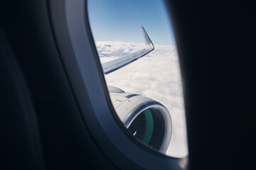 View through airplane window on wing with engine. Plane during flight above clouds.