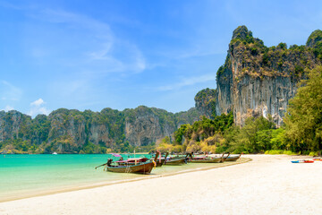 Railay beach west with exotic limestone cliff mountain and longtail wooden tourist boat, Krabi, Thailand