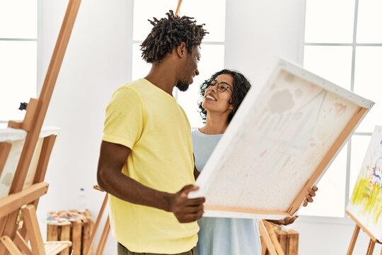 African american artist couple smiling happy holding canvas at art studio.