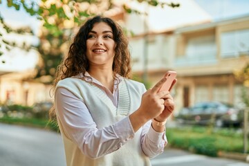 Young hispanic woman smiling happy using smartphone at the city.