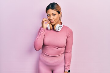 Beautiful hispanic woman wearing gym clothes and using headphones mouth and lips shut as zip with...