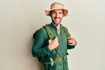 Handsome man with beard wearing explorer hat and backpack with a happy and cool smile on face....