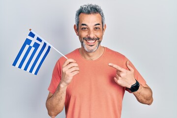 Handsome middle age man with grey hair holding greece flag smiling happy pointing with hand and finger