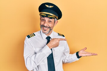 Handsome middle age man with grey hair wearing airplane pilot uniform amazed and smiling to the...