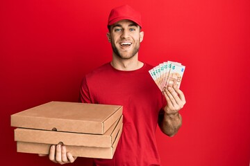 Young caucasian man holding take away food and 10 euros banknotes smiling and laughing hard out...
