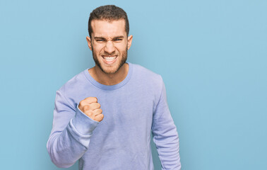 Young caucasian man wearing casual clothes angry and mad raising fist frustrated and furious while...