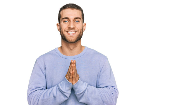 Young caucasian man wearing casual clothes praying with hands together asking for forgiveness smiling confident.