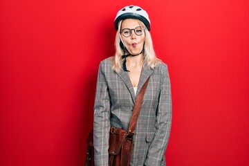 Beautiful caucasian blonde business woman wearing bike helmet making fish face with lips, crazy and comical gesture. funny expression.