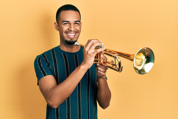 Young african american man playing trumpet celebrating crazy and amazed for success with open eyes screaming excited. - obrazy, fototapety, plakaty